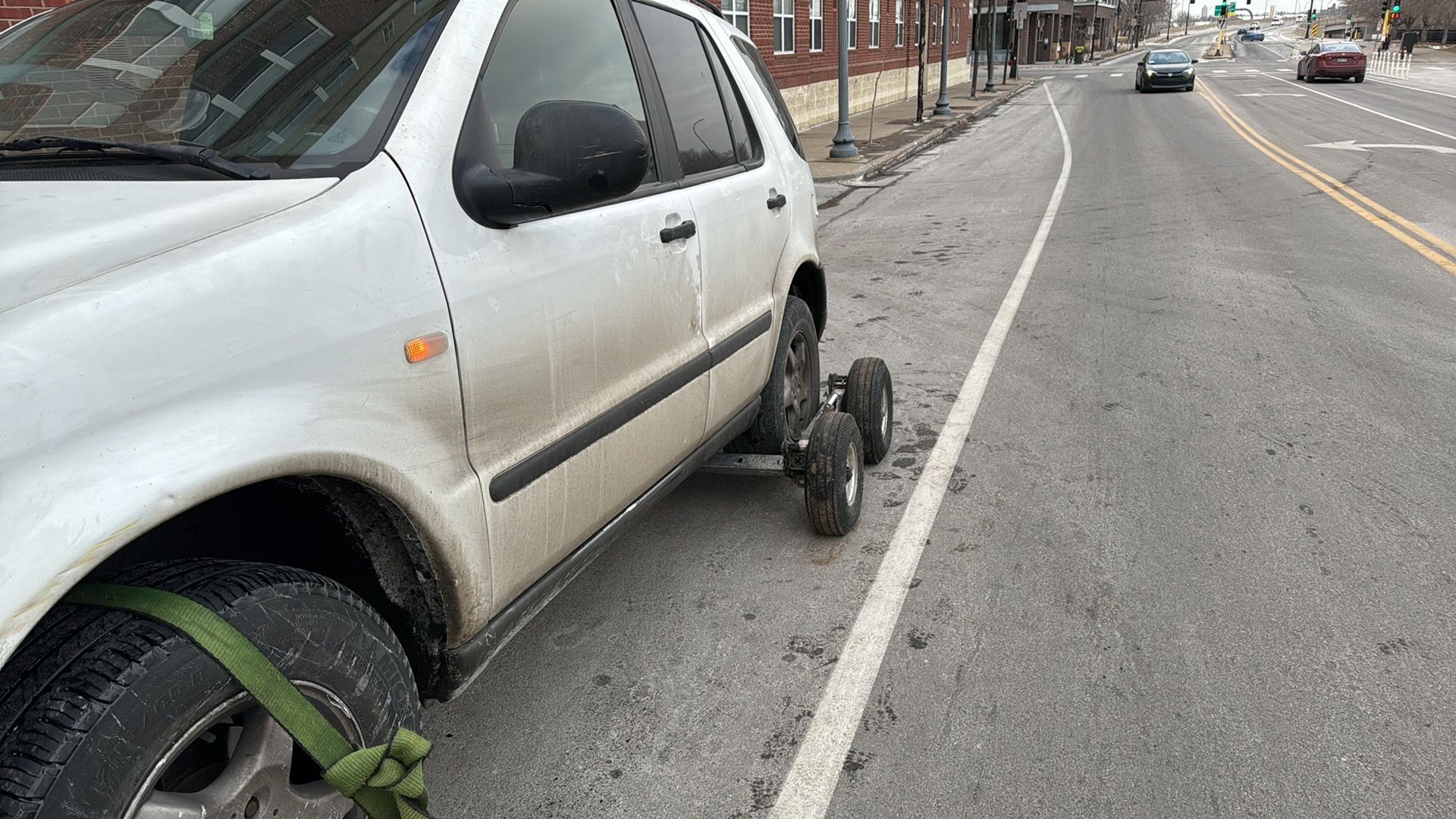 Silver car parked with a broken front wheel on a city street near the curb