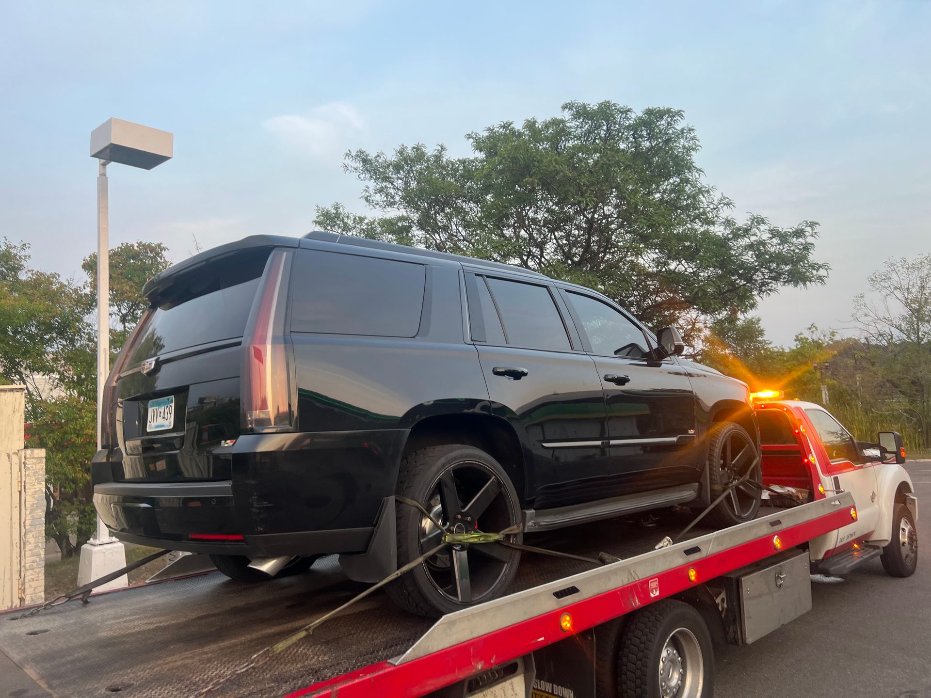 Black SUV being loaded onto a tow truck at dusk, with amber lights flashing.