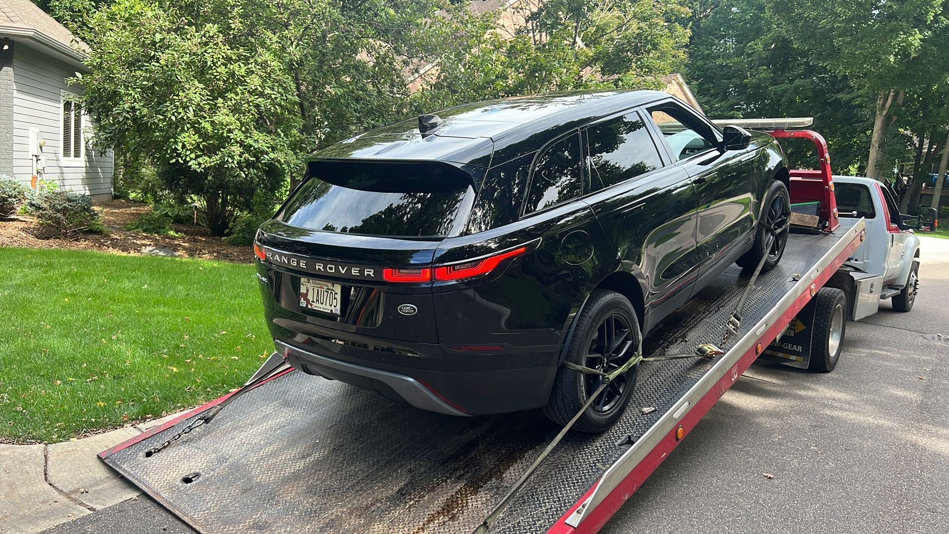 Black SUV loaded on a red tow truck ramp in a residential driveway