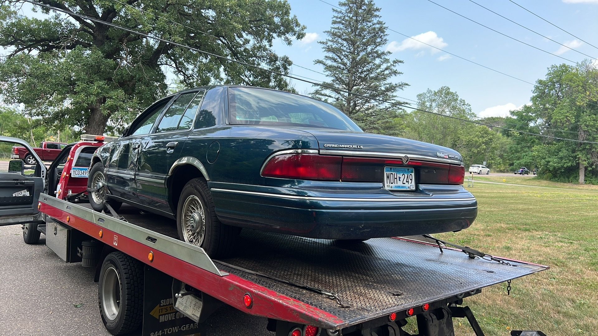 Dark green sedan on a red tow truck flatbed on a roadside.