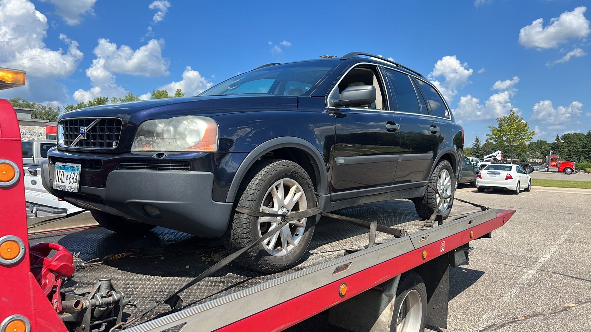 Black SUV on a tow truck flatbed under a bright blue sky in a parking lot