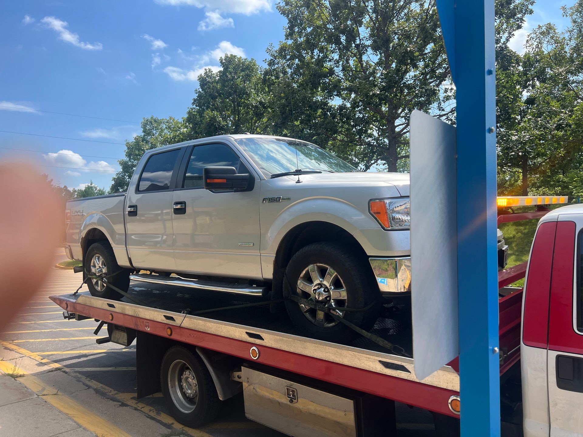 Silver pickup truck on a tow truck bed in a sunny parking lot