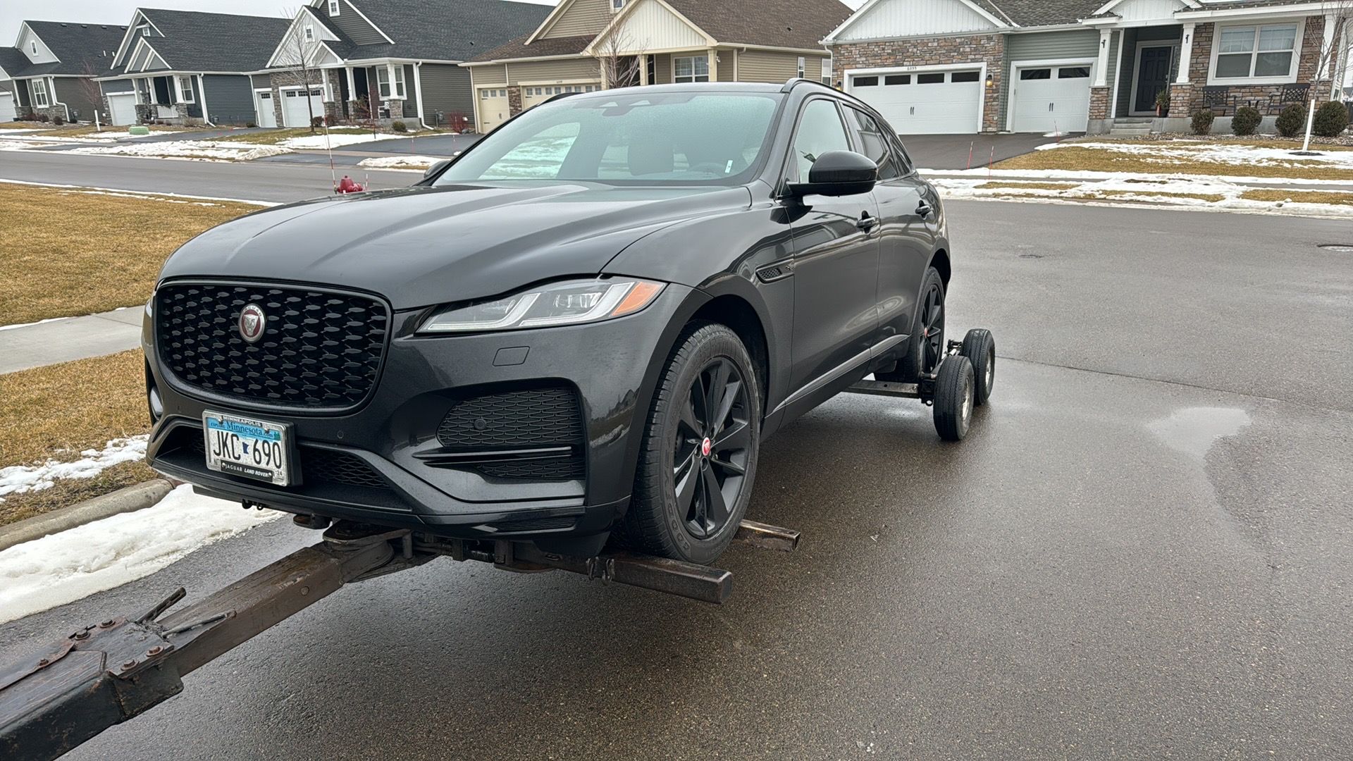 Black SUV parked on a wet residential street with patches of snow and houses in the background