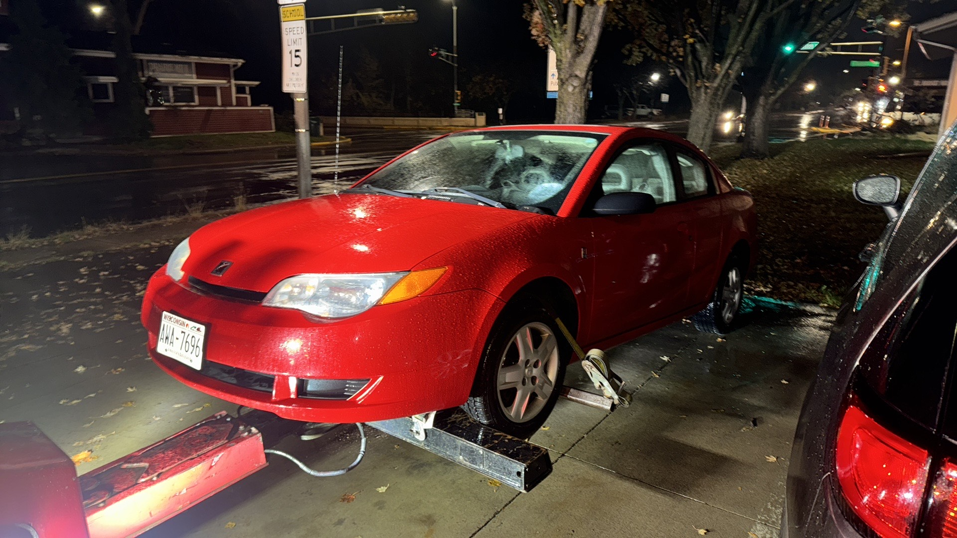 Red car crashed into a sidewalk sign at night, with broken glass around it.