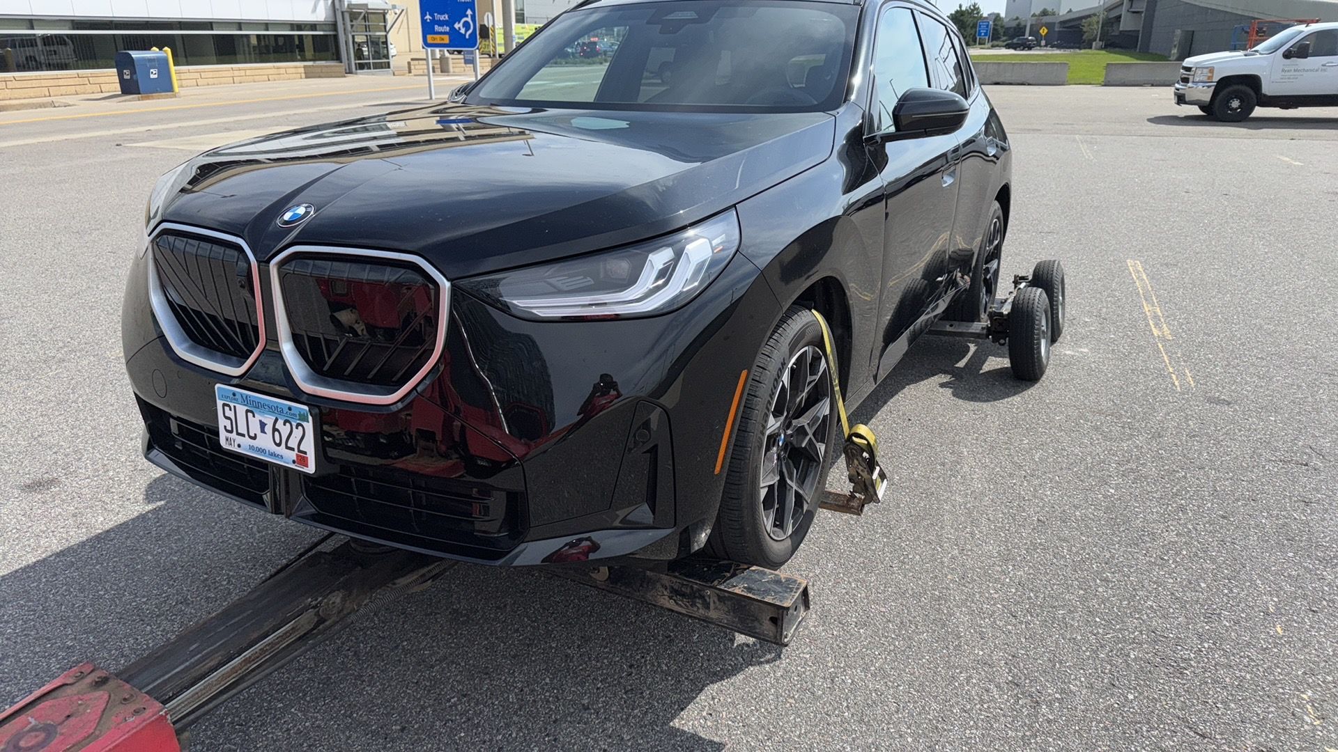 Black BMW sedan with damaged front wheel and bumper being towed on a flatbed truck