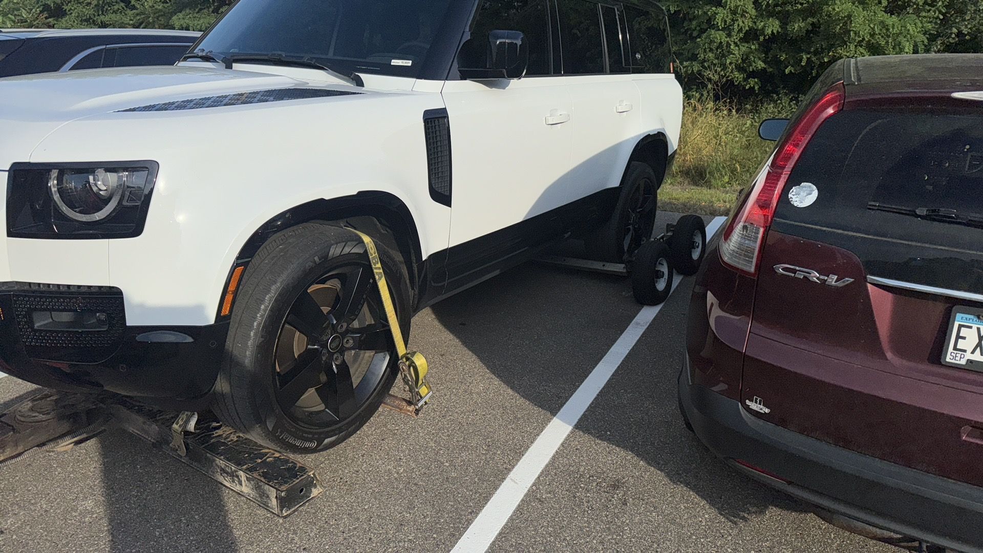 White SUV with yellow wheel clamps parked close to a maroon car in a parking lot.