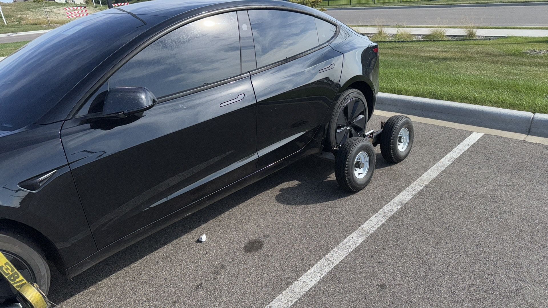 Black car parked in a lot with two rear tires mounted on small dollies or carts