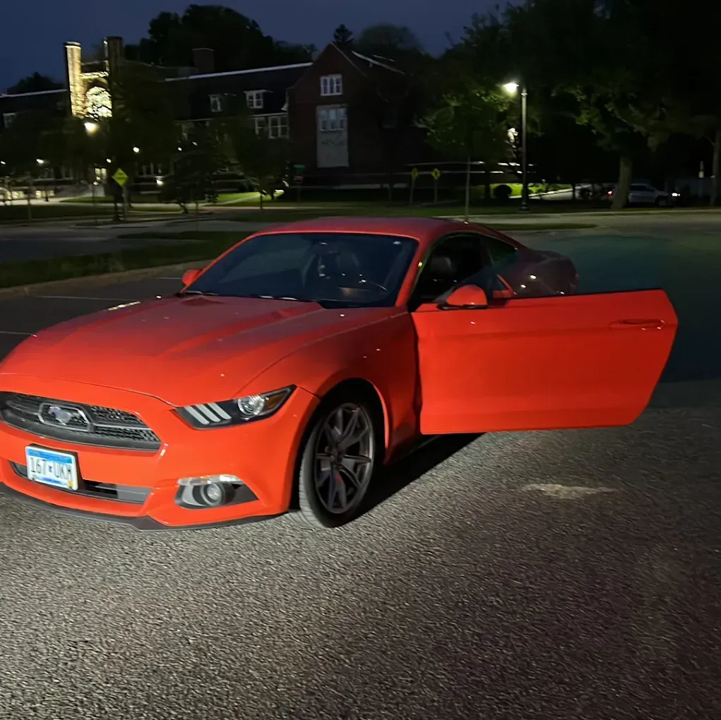 Red sports car parked at night with the driver’s door open in a lit lot