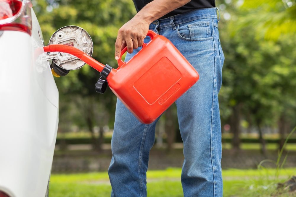 Person refueling a white car with a red gas can outdoors