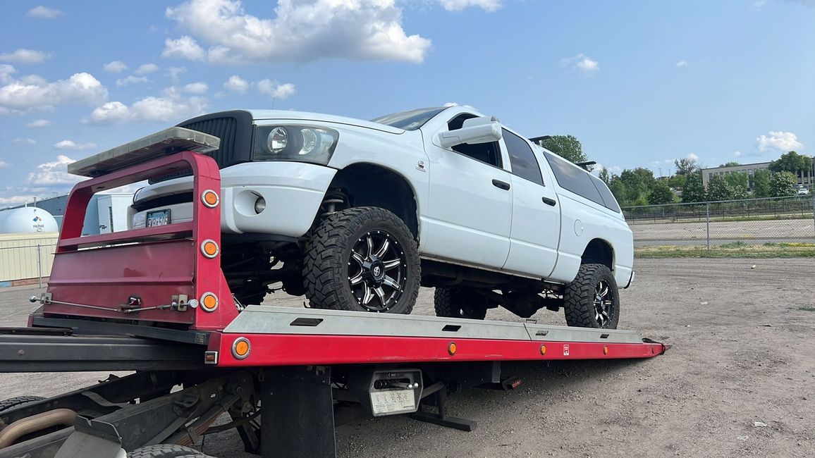 White pickup truck on a red tow trailer in a gravel lot under a cloudy sky