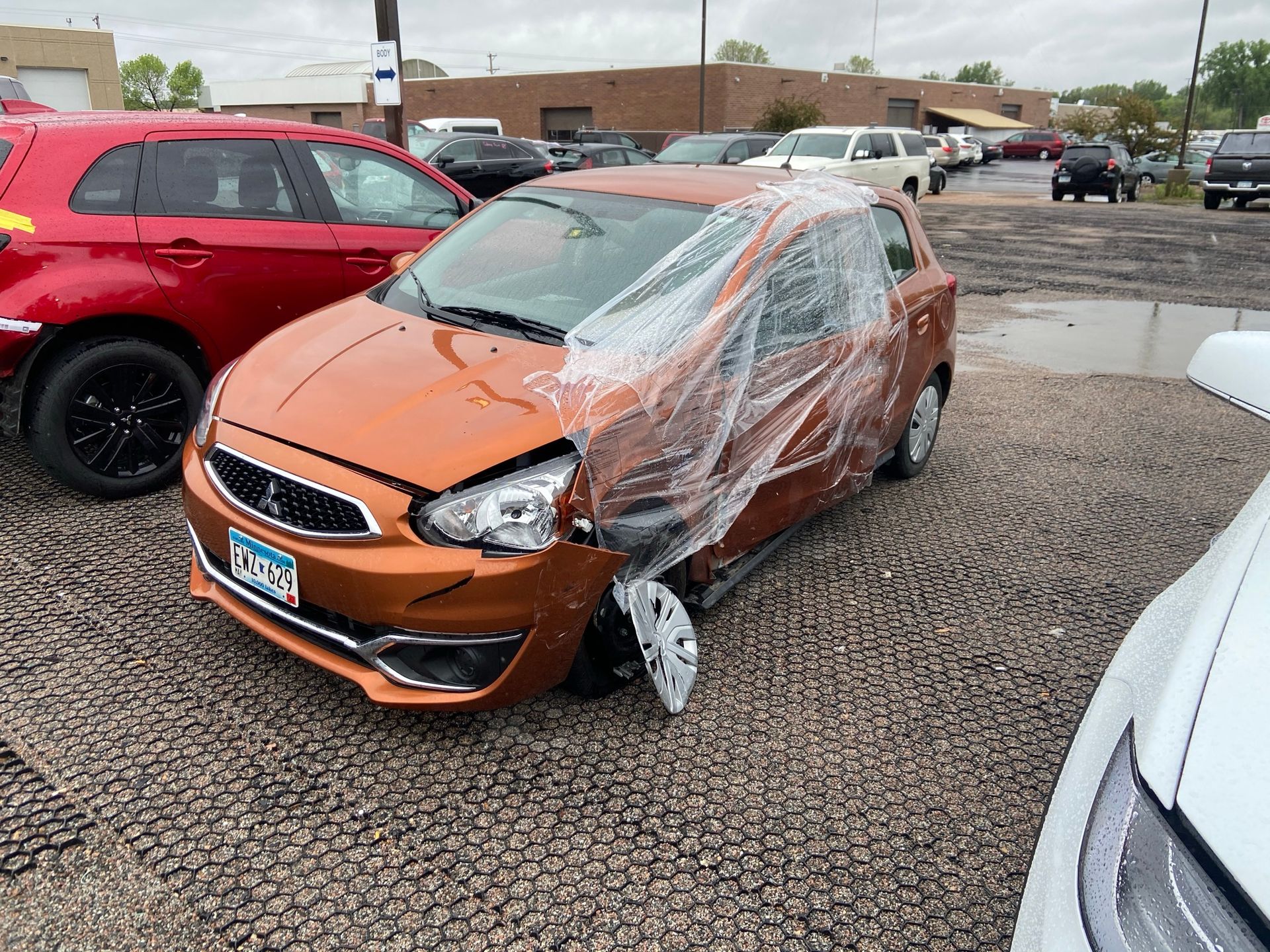 Orange car with heavy front-end damage and shattered windshield in a parking lot