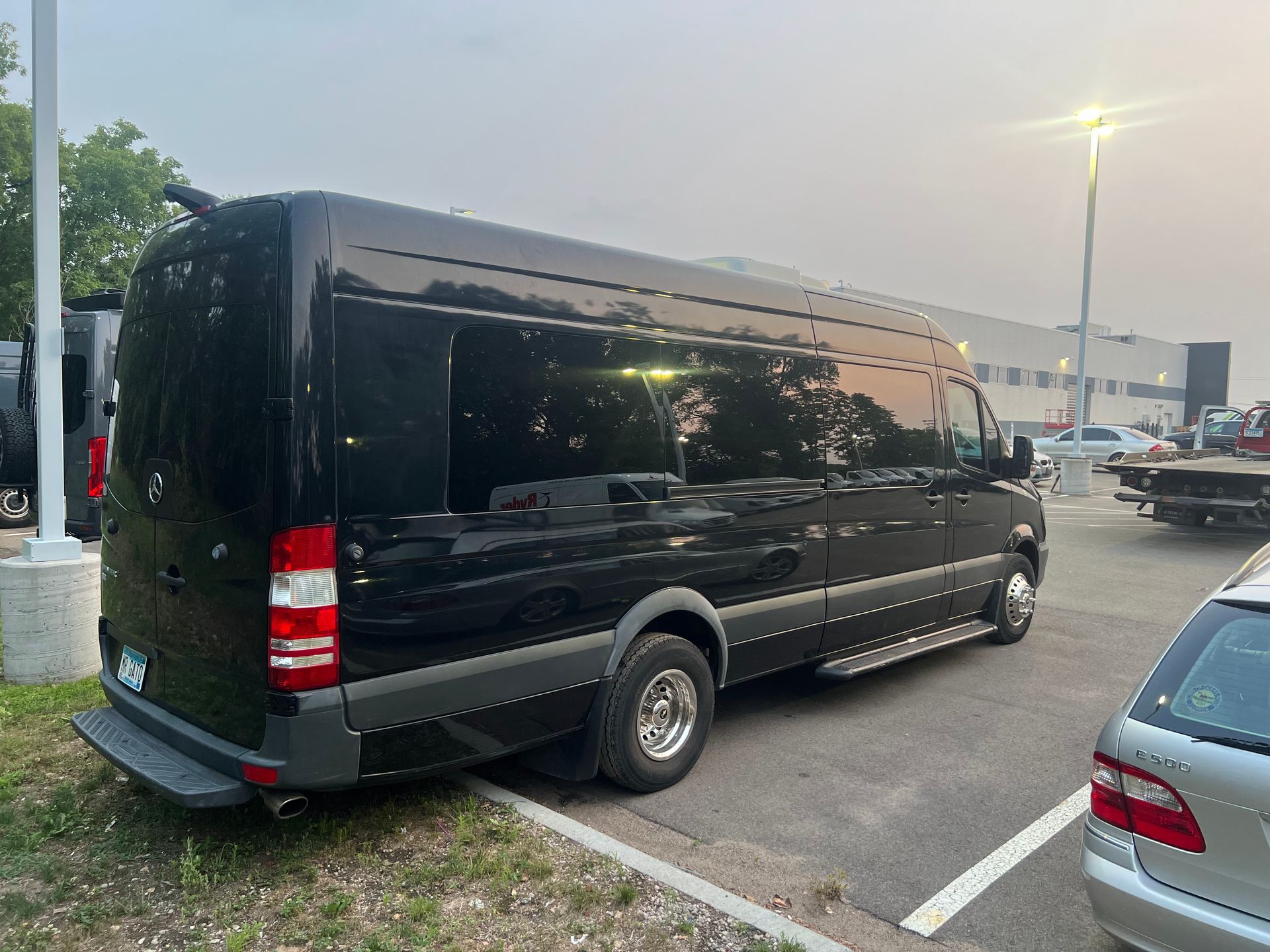 Black cargo van parked in a lot at dusk, seen from the rear-left side.