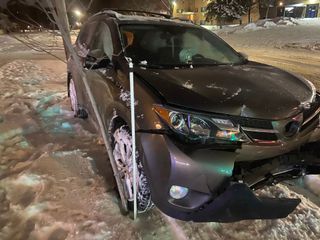 Gray sedan stuck in deep snow by the roadside at night, with a damaged front bumper.