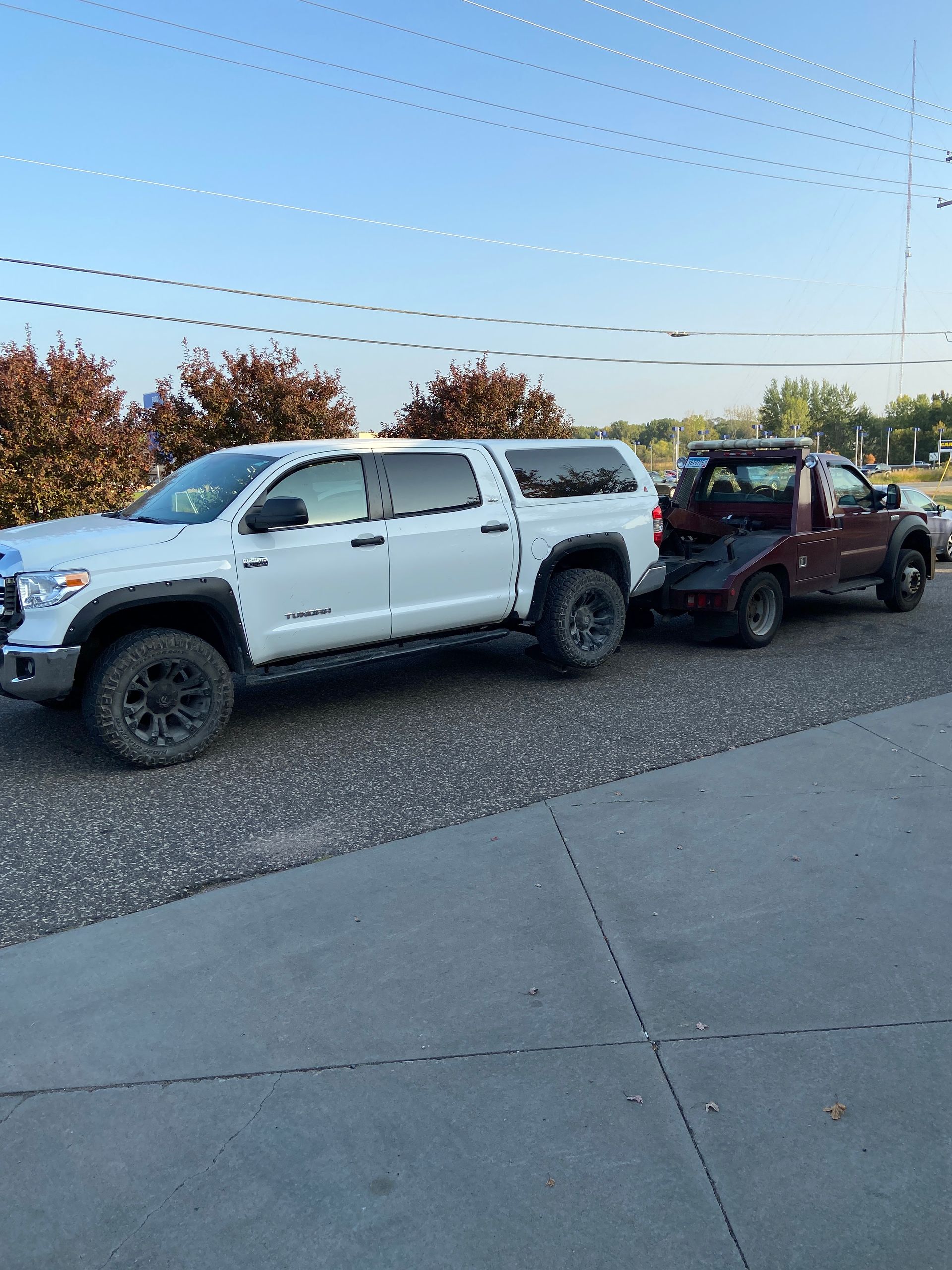 White pickup truck towing a red ATV on a trailer beside a gravel lot at dusk