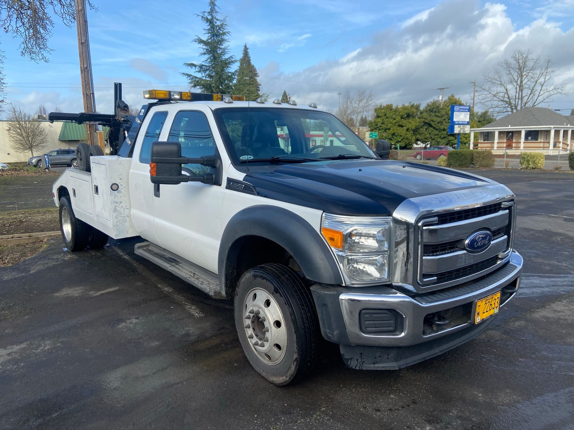 White utility pickup truck parked outdoors on a wet lot under a partly cloudy sky.