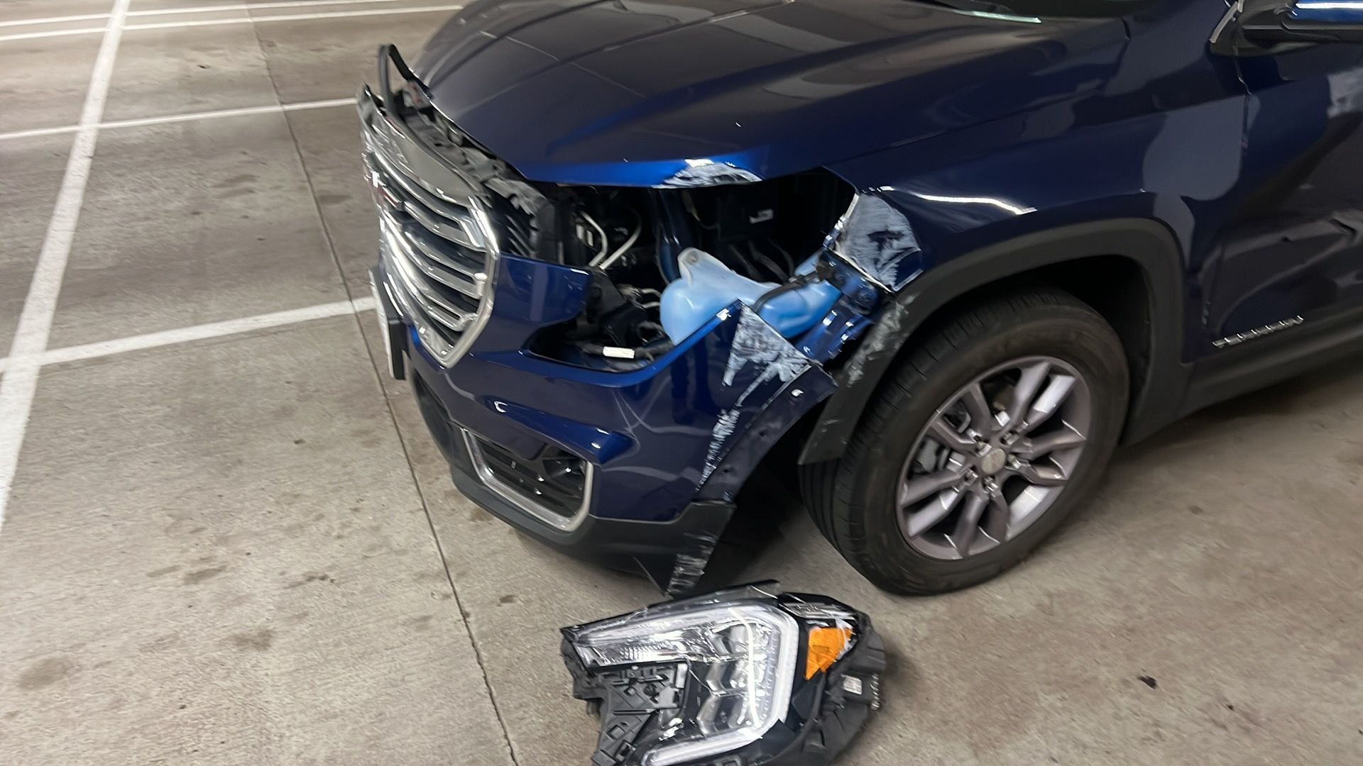 Damaged blue SUV front end with detached headlight in a parking garage
