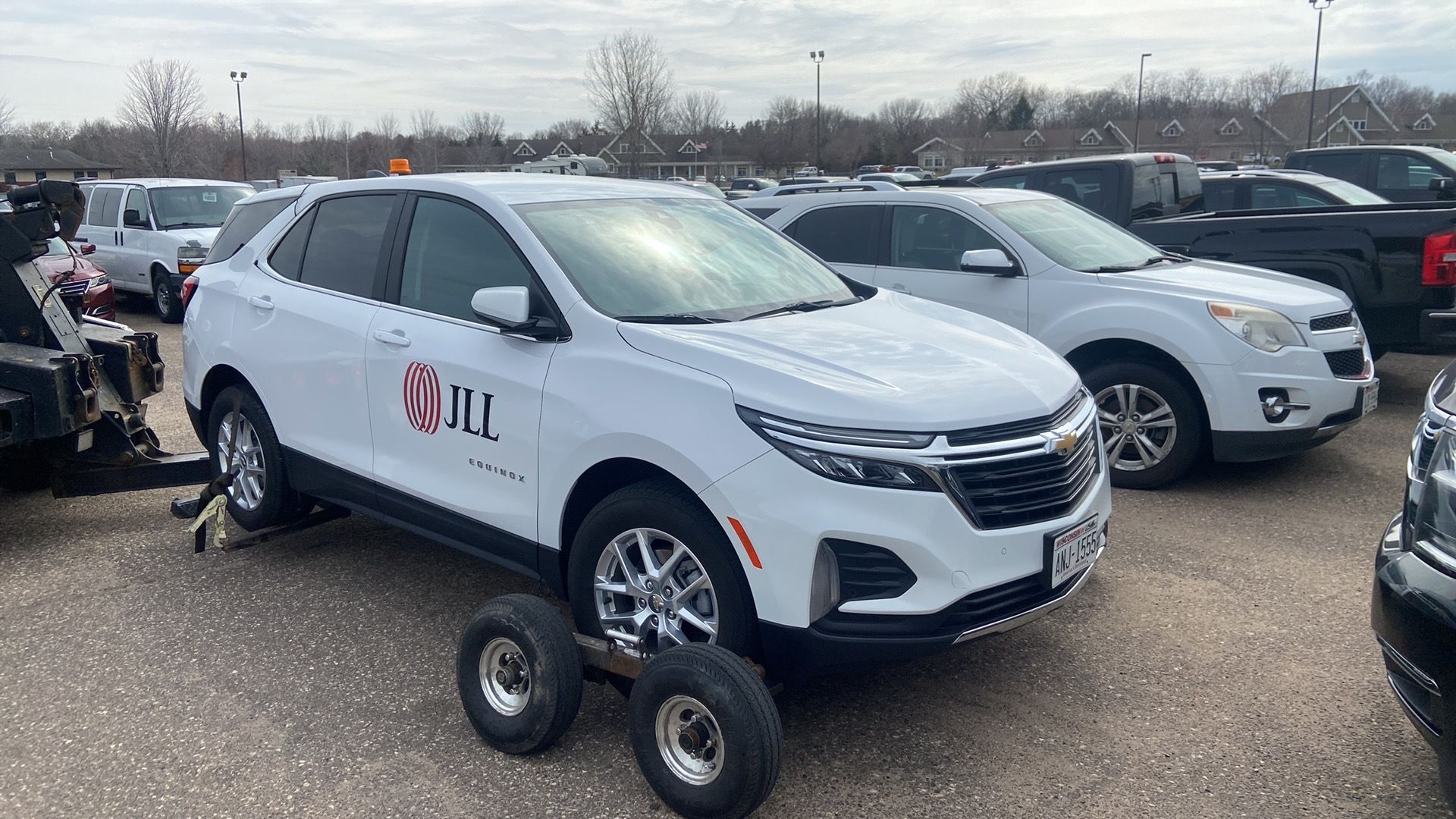 White SUV on a tow dolly in a parking lot, with other cars parked nearby.