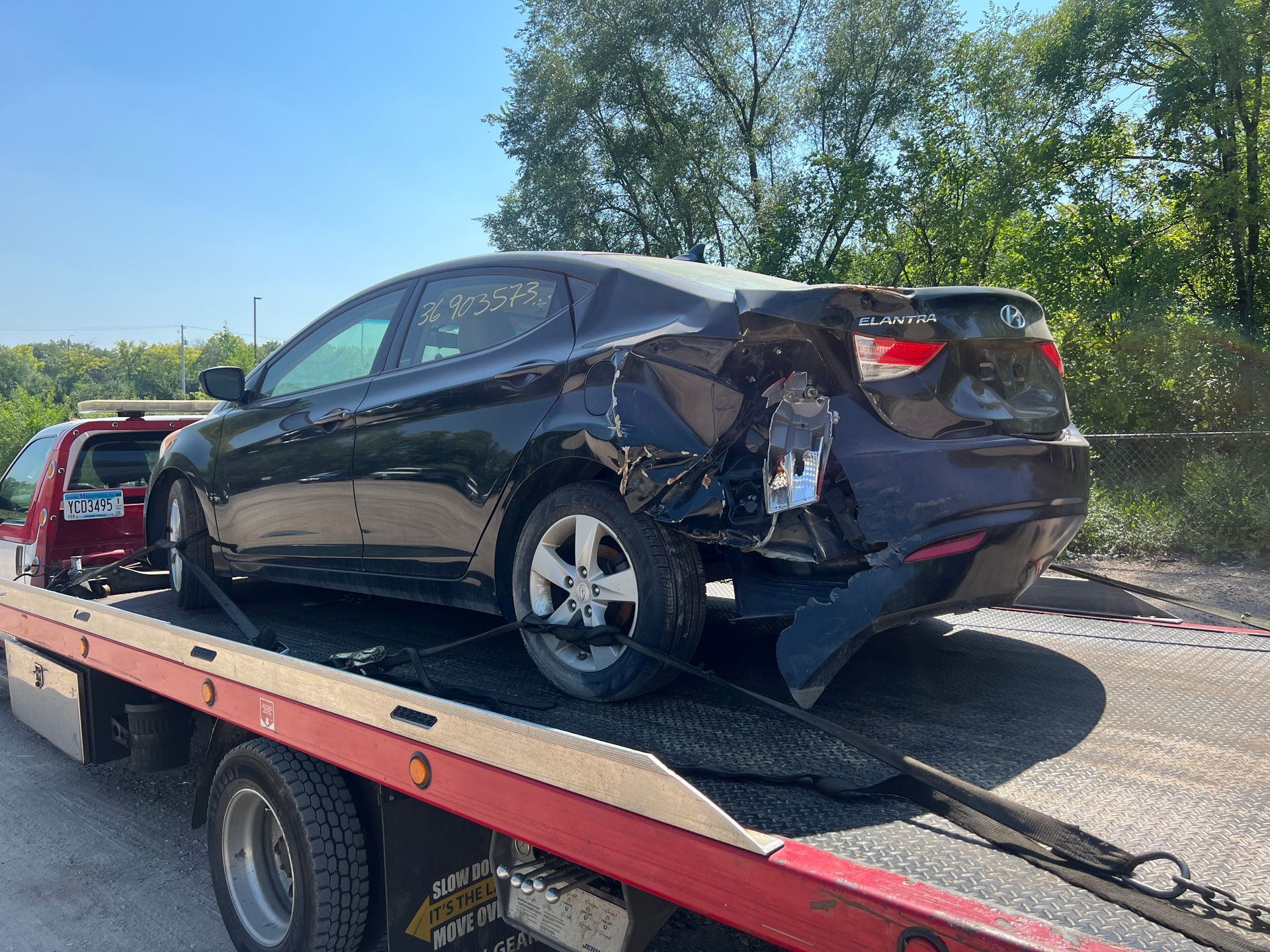 Damaged black sedan on a flatbed tow truck outdoors in daylight