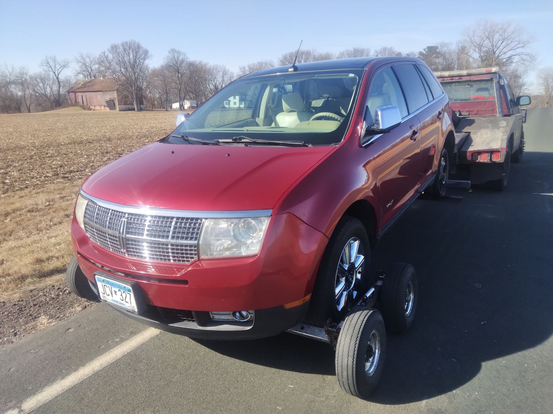 Red SUV stuck at an angle on a tow trailer beside a road in a rural area