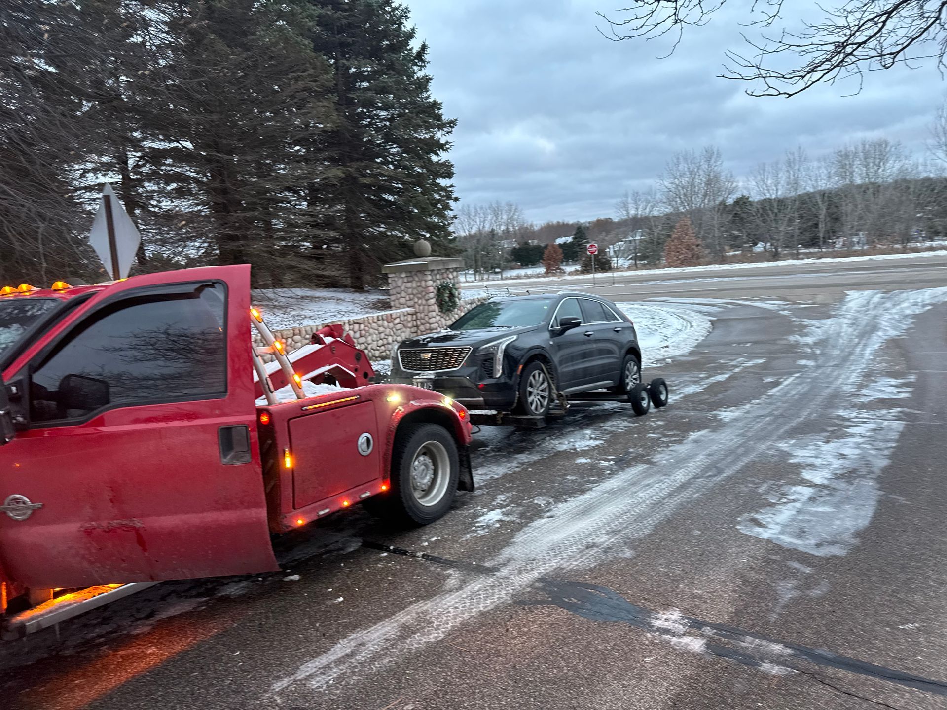 Red tow truck hauling a black SUV on a snowy roadside.