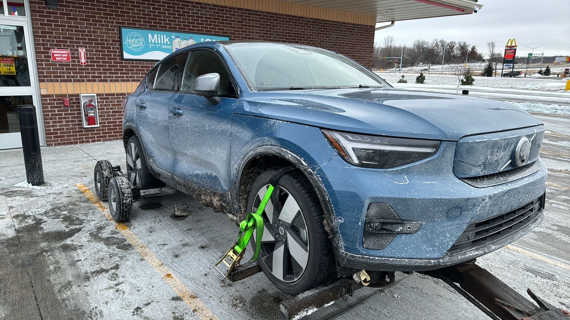 Blue SUV on a tow truck in a snowy parking lot, with a green wheel clamp attached to the front wheel.
