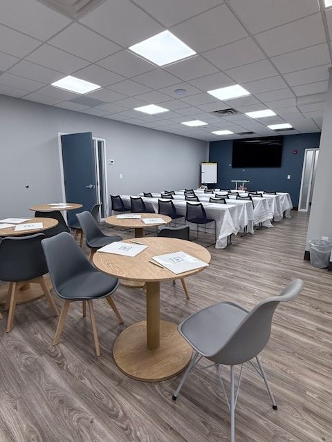 Meeting room with round tables and chairs, conference table, blue and gray walls, and overhead lighting.