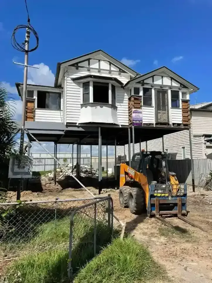 Raised weatherboard house supported by steel posts with earthmoving equipment onsite