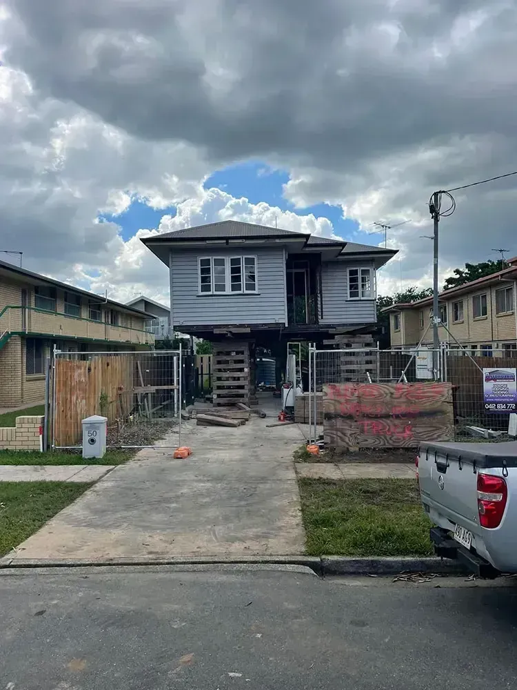 Elevated weatherboard house supported on timber cribbing during restumping work