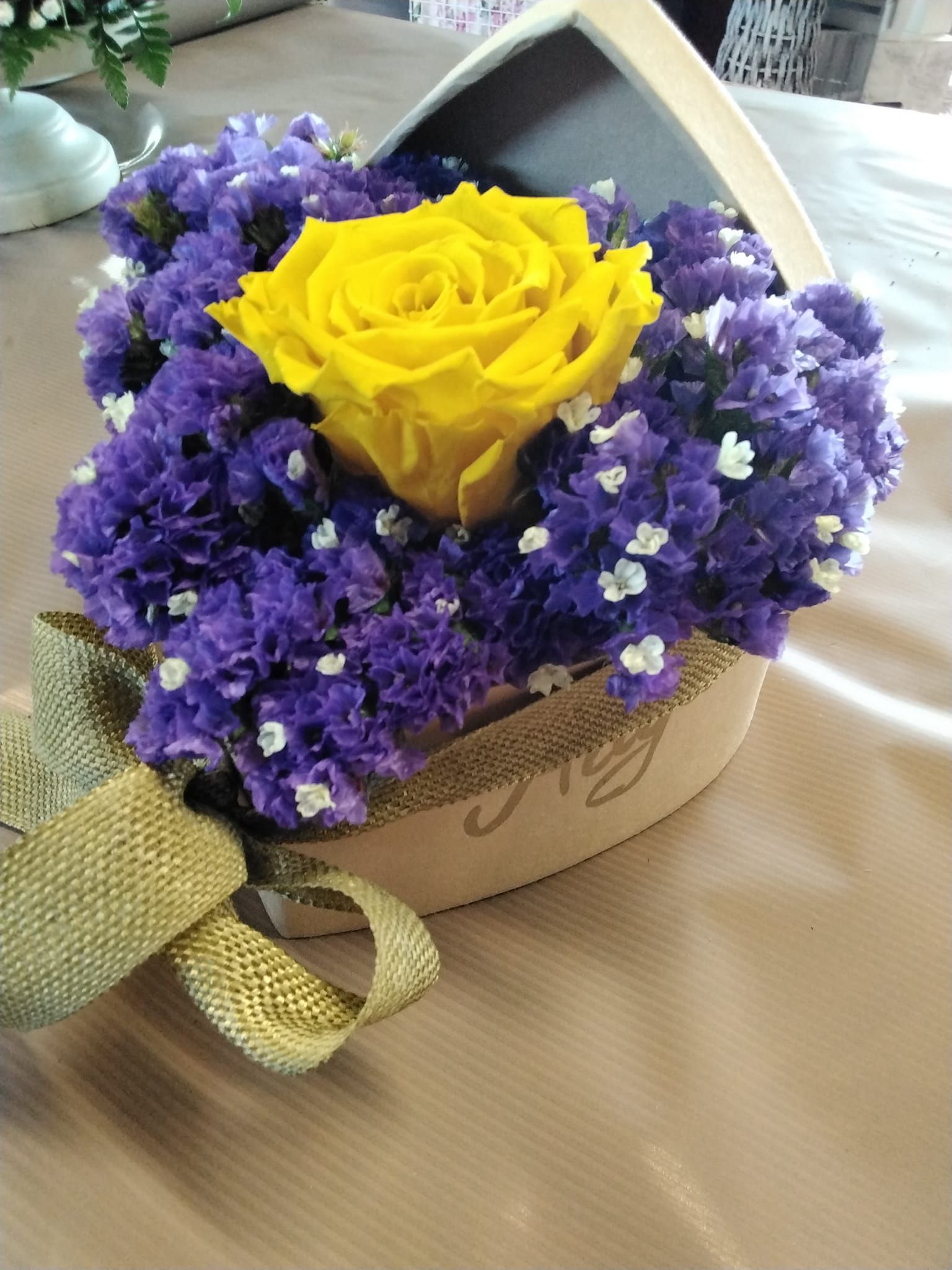 Una rosa gialla è circondata da fiori viola in una scatola