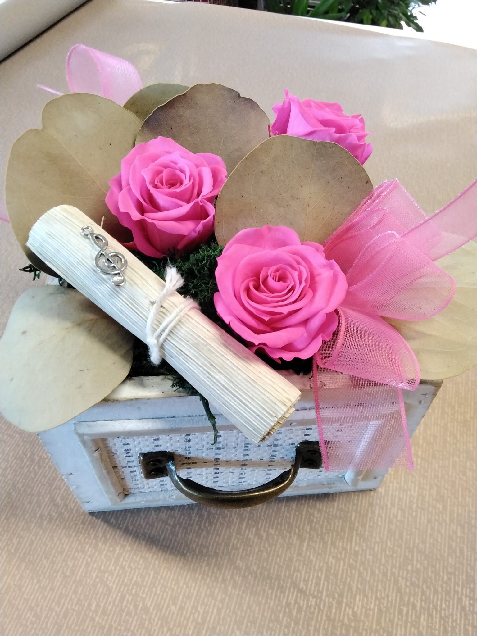 Una scatola piena di rose rosa e una pergamena su un tavolo.