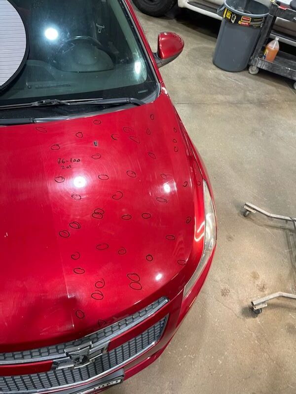 Red car hood with water droplets in an indoor garage, front grille visible