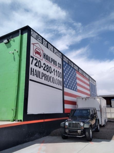 Moving truck with American flag mural and HALT-PCO.com text, parked beside a black jeep on a cloudy day