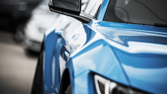 Close-up of a blue car’s front side and mirror, with another car blurred in the background