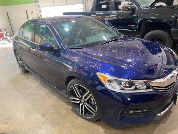 Blue Honda sedan parked indoors with water spots on the hood and windshield, next to a black pickup truck.