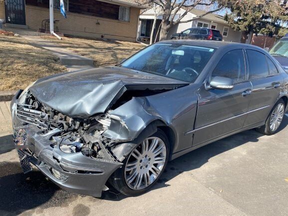 Silver sedan with severe front-end crash damage parked on a residential street
