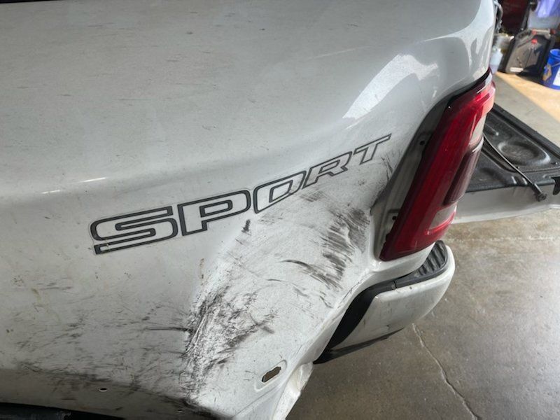 White pickup truck rear quarter panel with a large black scrape and dent near the taillight