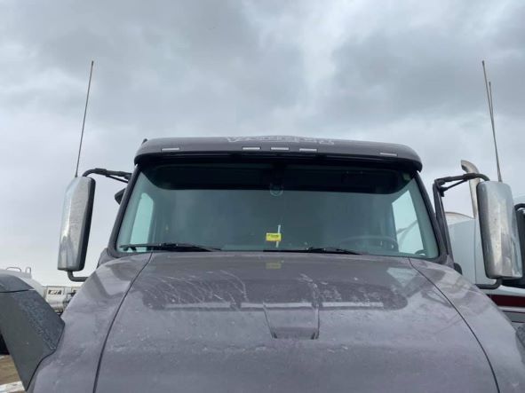 Front view of a dark gray semi-truck with side mirrors and antennas against a cloudy sky