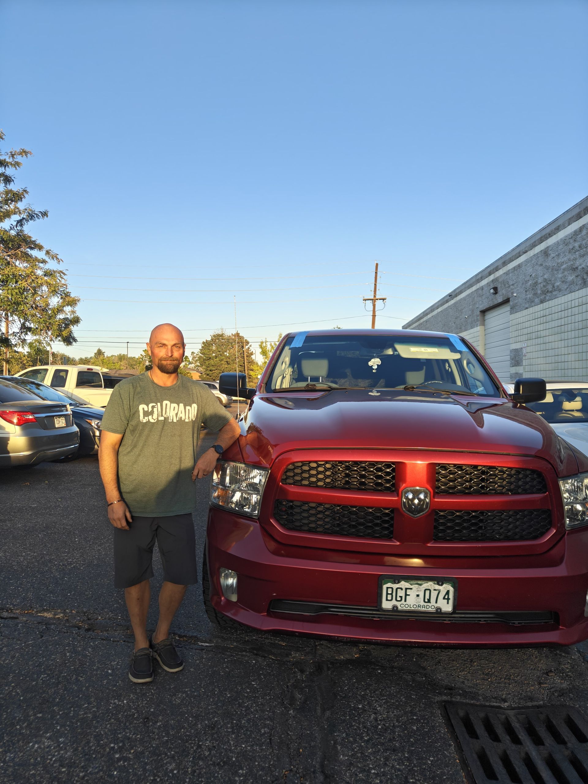 Man standing beside a red Ram truck in a parking lot beside a building.