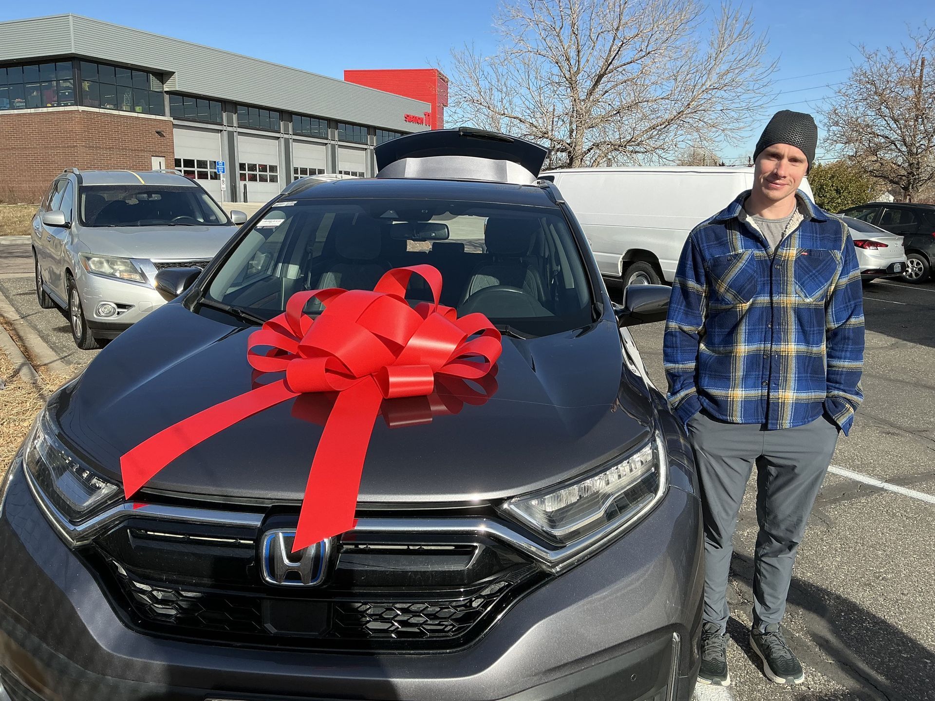 Gray Honda SUV with a large red bow, parked outside a building, with a person standing beside it.