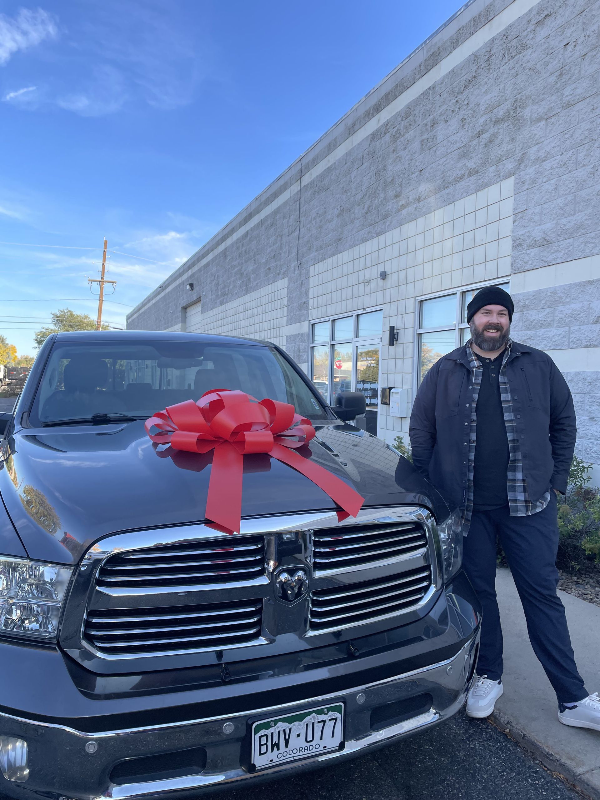 Man standing beside a black pickup truck with a large red bow in front of a building