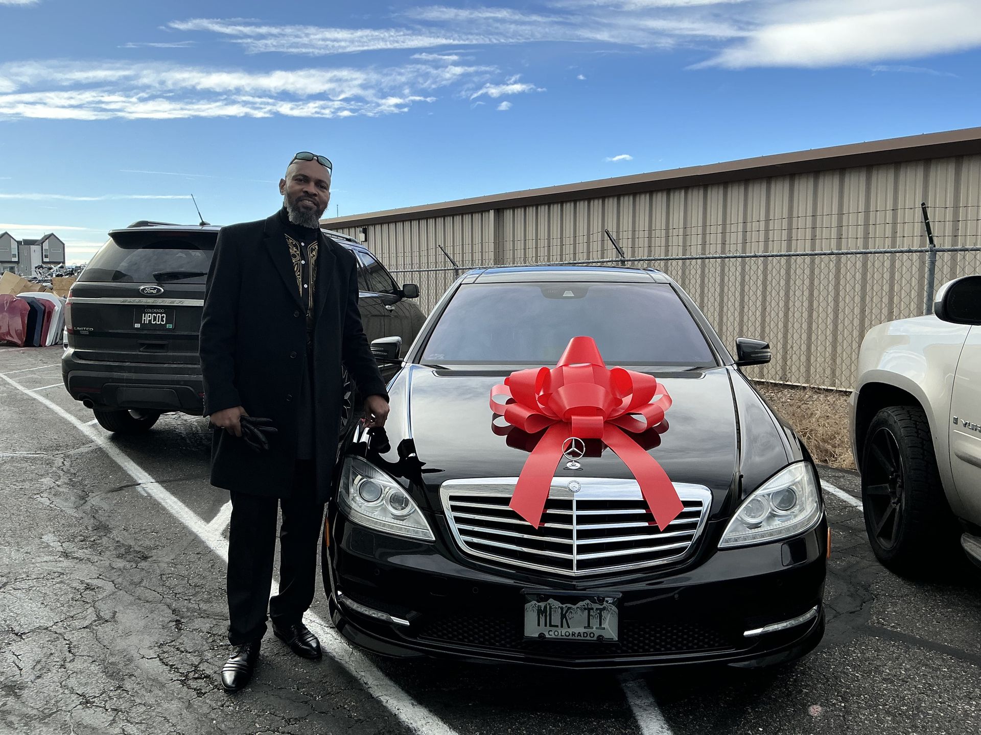 Man standing beside a black sedan with a large red bow in a parking lot