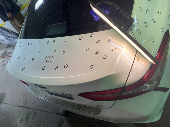 White hatchback car rear covered in raindrops, parked indoors under bright lights.