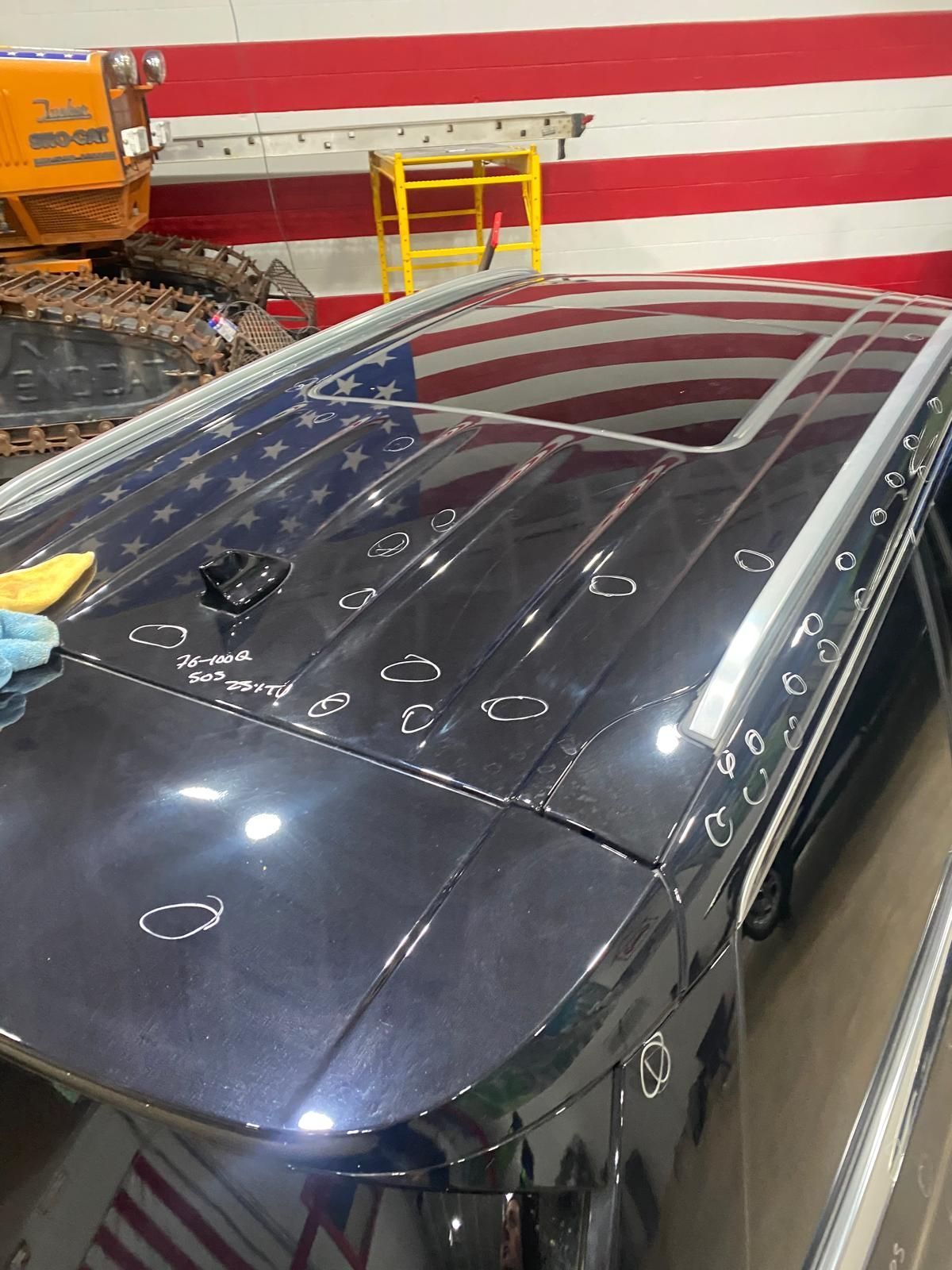 Black car roof with many paint-mark circles in a workshop beside red-and-white striped wall