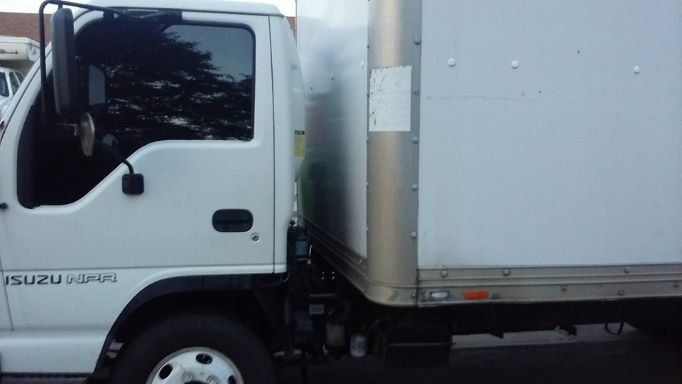 White Isuzu box truck parked outdoors, side view with cab and cargo box visible