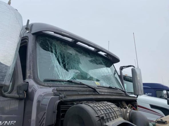 Damaged black truck with shattered windshield and snow on the cab at a snowy roadside