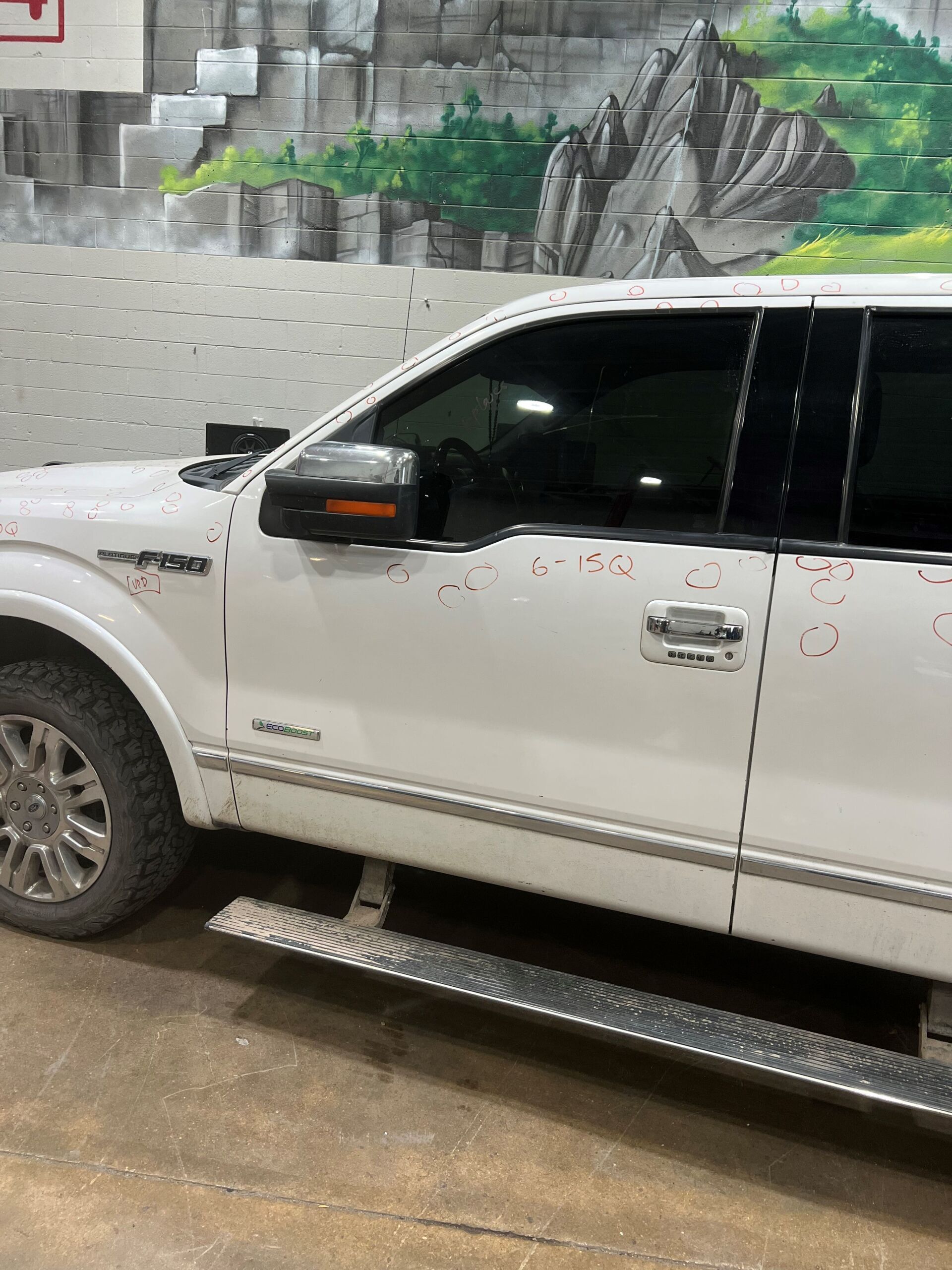 White pickup truck parked indoors against a mural wall, with running boards and tinted windows.