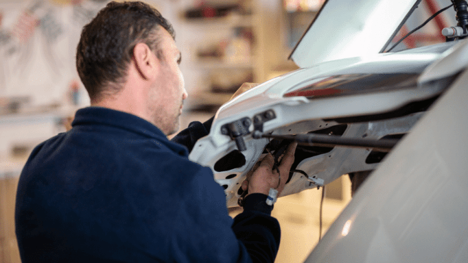Technician inspecting wiring beneath a white vehicle in a garage