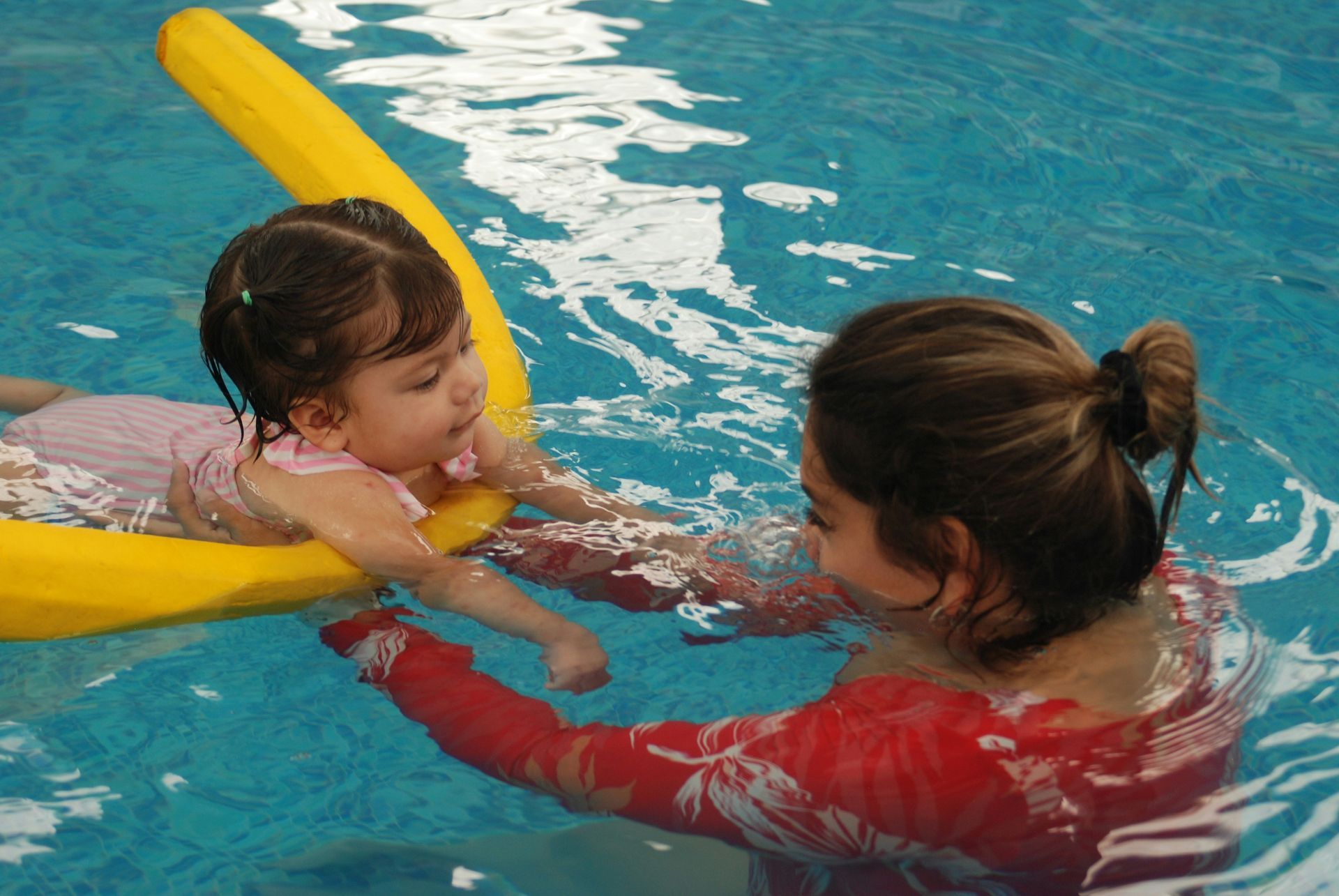 A mother helps her child swim with a pool noodle