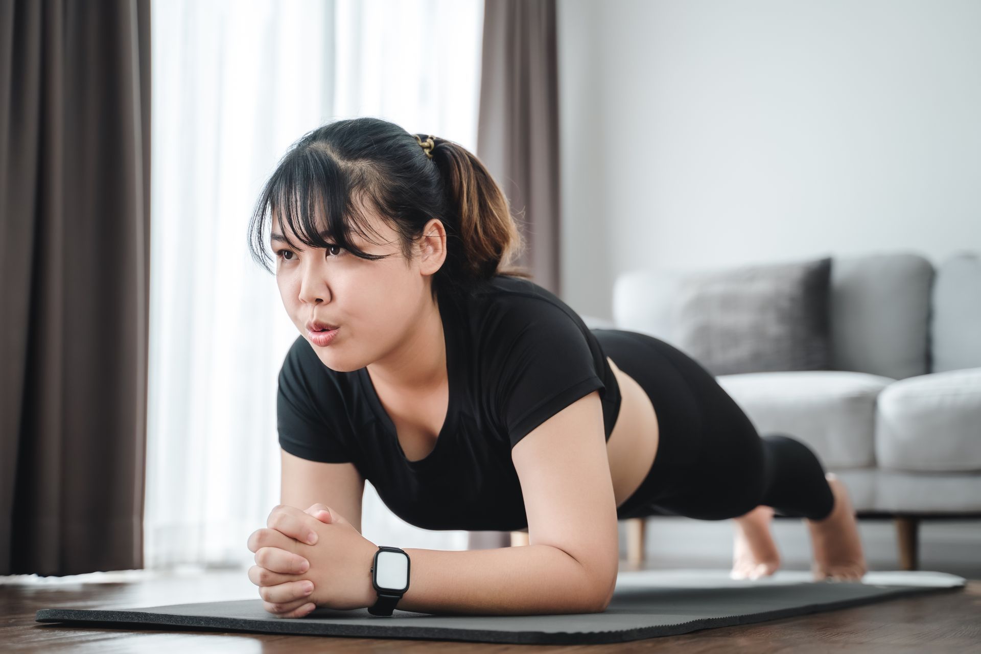 Woman performing a plank exercise on a yoga mat in a home living room.