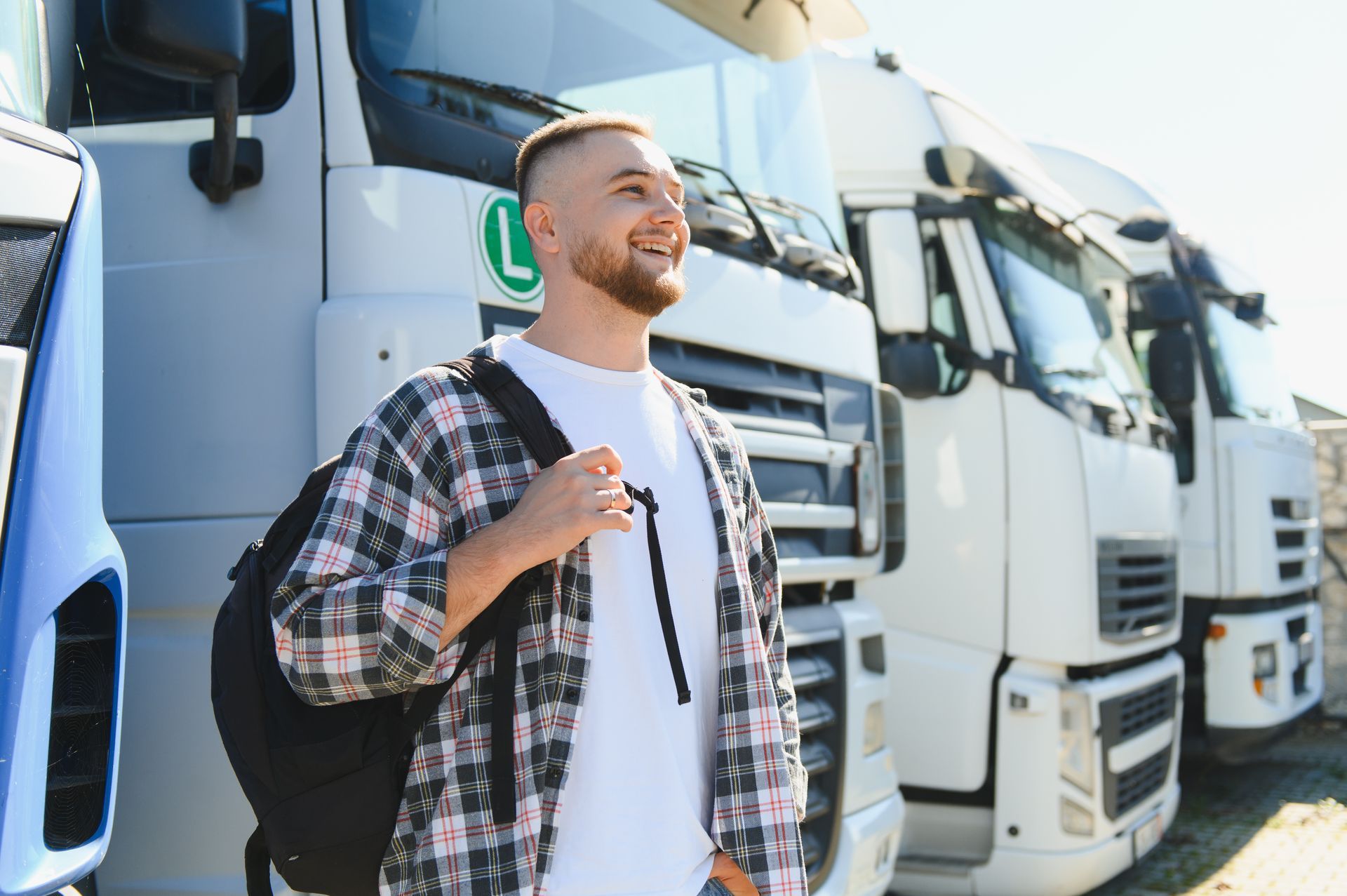 A man, hopeful and smiling, is looking at the distance with heavy vehicles lined-up behind him.